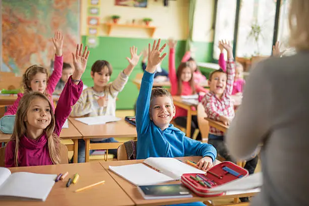 Large group of school children raising their hands ready to answer the question.